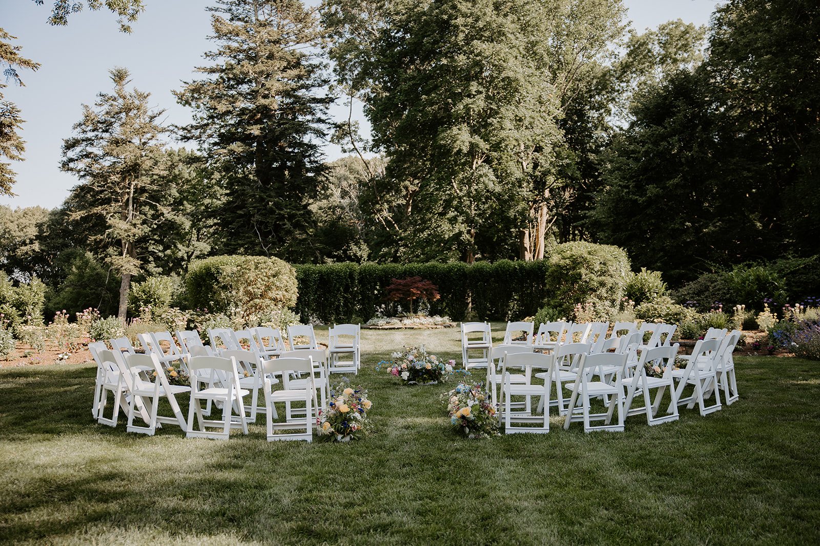 White chairs and pastel flowers set for Jim and Anne’s lawn ceremony at Glen Manor House, Portsmouth RI